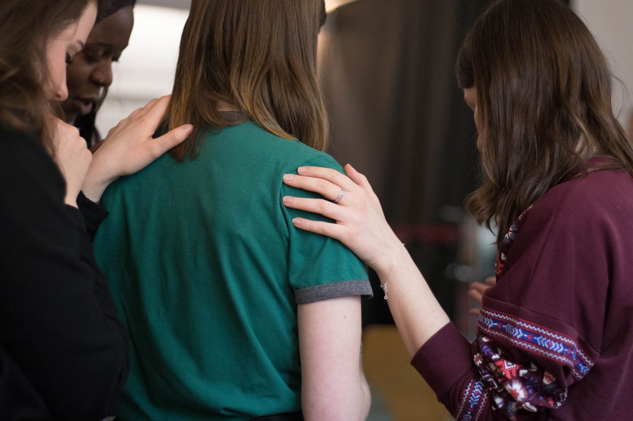 Women from different backgrounds laying hands on one another in prayer